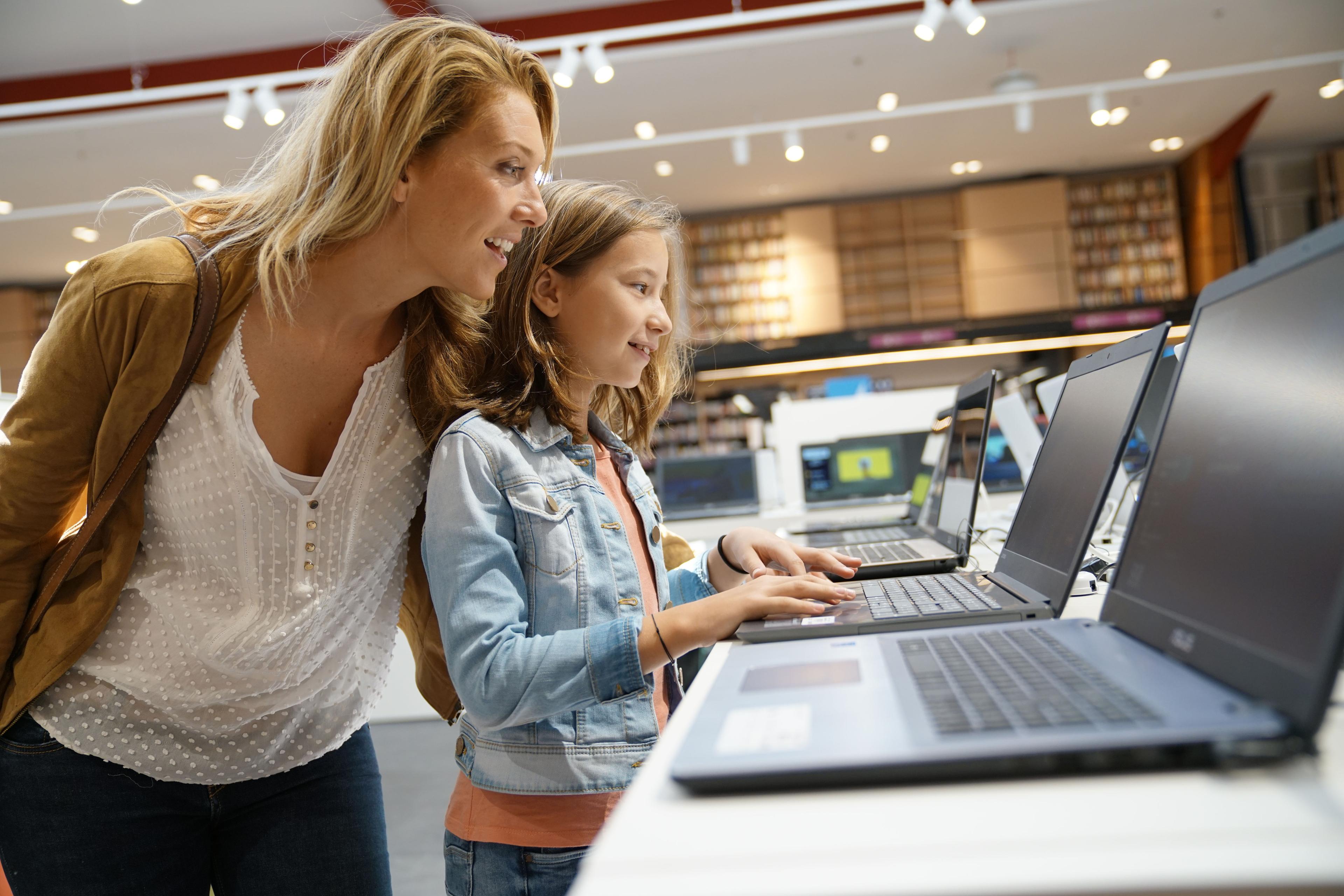 A woman and a child are looking at a laptop in an electronic store. This shows how Acima Leasing is useful during the back-to-school season.
