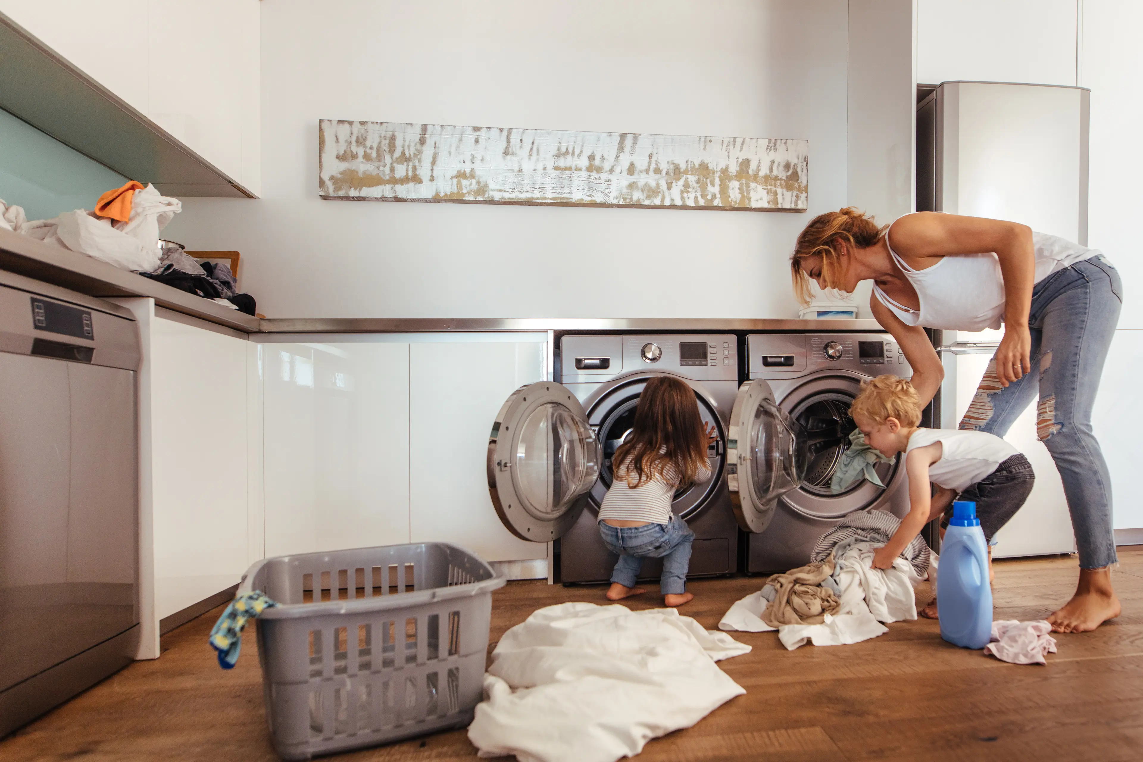 A woman and two kids happily do laundry together. The woman smiles while teaching the kids, who eagerly help. The scene captures how Acima Leasing can help customers get the appliances they need.